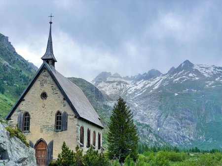 Photo for COPY SPACE: Stunning glaciers tower above a historic Catholic church in the Swiss Alps. Spectacular shot of dark clouds gathering above an ancient chapel in the picturesque mountains of Switzerland. - Royalty Free Image