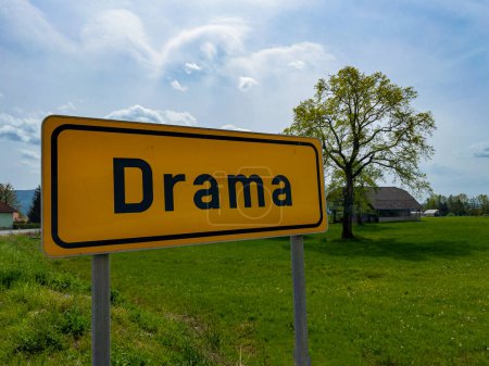 Téléchargez les photos : CLOSE UP: A yellow traffic sign indicates you are entering the amusingly named town of Drama in Slovenian countryside. Funny shot of a signpost showing traffic they are arriving into Drama village. - en image libre de droit