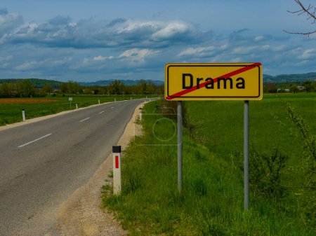 Photo for Empty asphalt road running across the idyllic Slovenian countryside and leads past a yellow traffic sign signalling the end of Drama village. Road sign denoting the end of Drama town in rural Slovenia - Royalty Free Image