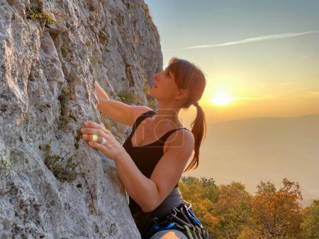 Téléchargez les photos : Athletic Caucasian young woman climbs up a rock wall in Crni Kal at golden fall sunrise. Fit female rock climber training in Slovenian countryside on a sunny autumn evening. - en image libre de droit