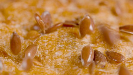 Téléchargez les photos : MACRO, DOF: Shiny brown seeds are scattered across the crust of a loaf of delicious whole-wheat bread. Detailed close up shot of the crispy crust of an unleavened bread sitting on the dining table. - en image libre de droit