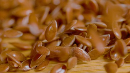 Photo for MACRO, DOF: Detailed shot of tiny flaxseeds falling onto the wooden kitchen table. Reddish brown hued linseeds bounce around and get scattered across the wood countertop. Shiny flax seeds falling down - Royalty Free Image