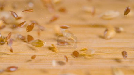 Photo for MACRO, DOF: A mix of dried wheat, sesame and shiny brown flax seeds gets scattered across the wooden dining table. High detail view of tiny cereal seeds bouncing across the empty kitchen countertop. - Royalty Free Image