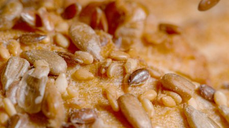 Photo for MACRO, DOF: Reddish brown hued linseeds fall on the crust of a fresh homemade rustic unleavened bread. Cinematic shot of shiny seeds being scattered across a loaf of delicious whole-wheat bread. - Royalty Free Image