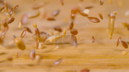 Photo for MACRO, DOF: High detail view of tiny cereal seeds bouncing across the empty kitchen countertop. A mix of dried wheat, sesame and shiny brown flax seeds gets scattered across the wooden dining table. - Royalty Free Image