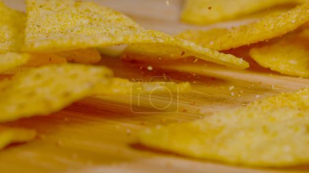 Téléchargez les photos : MACRO, DOF: Triangular shaped golden colored tortilla chips fall onto the wooden surface. Tortilla crisps sprinkled with sea salt and fragrant mexican spices get scattered across the dining table. - en image libre de droit