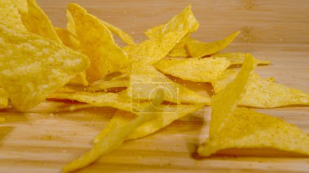 Photo for CLOSE UP, DOF: Tortilla crisps sprinkled with sea salt and fragrant mexican spices get scattered across the dining table. Triangular shaped golden colored tortilla chips fall onto the wooden surface. - Royalty Free Image