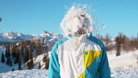 Foto de CLOSE UP: Cheerful Caucasian guy on a fun snowboarding trip in Slovenia gets hit by a big snowball. Smiling male on active vacation in the picturesque Slovenian Alps gets caught in a snow fight. - Imagen libre de derechos