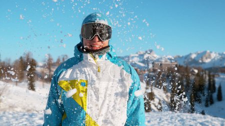 Foto de CLOSE UP: Smiling male on active vacation in the Slovenian Alps gets caught in a random snow fight. Cheerful Caucasian guy on a fun snowboarding trip in Vogel, Slovenia gets hit by a big snowball. - Imagen libre de derechos