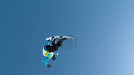 Téléchargez les photos : Man snowboarding in the Chinese mountains performs a spectacular flip while riding in adrenaline park. Fearless young male snowboarder does a breathtaking backflip after jumping off a massive kicker. - en image libre de droit