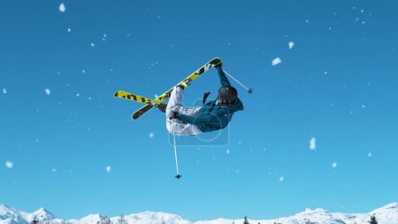 Foto de Athletic male tourist freestyle skiing in the Slovenian Alps jumps into the air and performs a grab trick. Spectacular shot of a young male snowboarder jumping off a kicker and doing a massive stunt. - Imagen libre de derechos