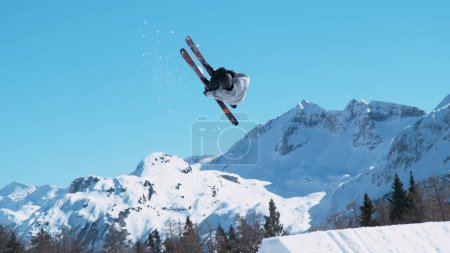 Foto de Spectacular shot of an extreme skier jumping off a kicker and doing a beautiful backflip. Athletic male tourist freestyle skiing in the Japanese mountains does a flip trick on a sunny winter day. - Imagen libre de derechos