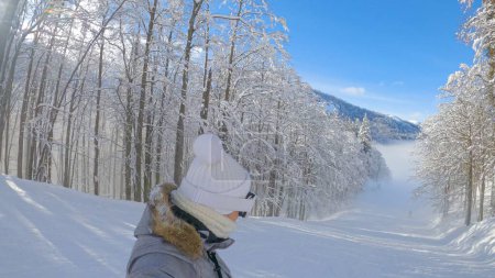 Foto de SELFIE: Mujer joven de vacaciones activas en las tablas de snowboard de los Alpes Julianos a lo largo de una pista de esquí brumosa. Mujer snowboarder cruceros a lo largo de una pendiente arreglada en un día de invierno soleado. Chica montando en Eslovenia. - Imagen libre de derechos