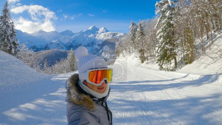 Photo for SELFIE: Smiling Caucasian female snowboarder cruises along a groomed slope on a sunny winter day. Young woman on active vacation in the Julian Alps snowboards along a scenic ski resort trail in Alps. - Royalty Free Image