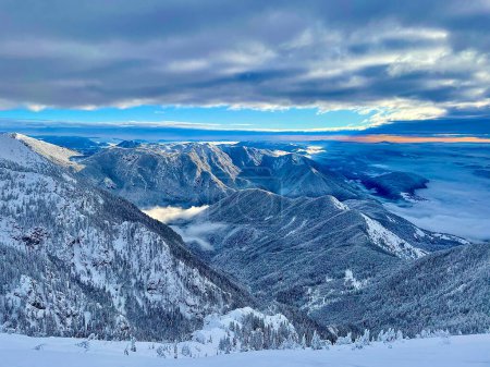 Téléchargez les photos : Breathtaking view of the wintry valley and rocky mountains of the Julian Alps on a beautiful January morning. Sunset illuminates the snowy mountain ranges and coniferous woods in rural Slovenia. - en image libre de droit