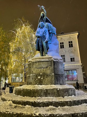 Photo for VERTICAL: Historic bronze statue of Preseren and his muse is covered in fresh snow. Festive Christmas lights illuminate the snowy monument in the middle of Preseren square, Ljubljana on a cold night. - Royalty Free Image