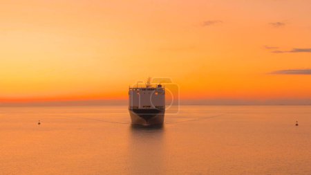 Photo for AERIAL: Large freight ship is transporting heavy cargo at gorgeous golden sunset. Spectacular drone shot of a freight carrier ship as it transports merchandise at sunset. Flying near industrial vessel - Royalty Free Image