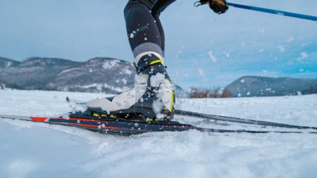 Téléchargez les photos : LOW ANGLE, CLOSE UP, DOF: Professional nordic skiing athlete pushes off her ski and poles while training in snowy mountains of Slovenia. Unrecognizable woman trains nordic skiing in wintry Bohinj. - en image libre de droit