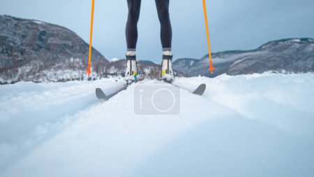 Téléchargez les photos : LOW ANGLE, CLOSE UP, DOF: Young Caucasian woman nordic skiing in the Slovenian mountains pushes herself along the tracks. Unrecognizable female athlete skis along tracks running around training center - en image libre de droit