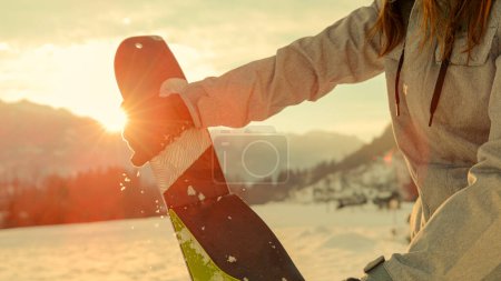 Foto de CLOSE UP, LENS FLARE, DOF: Active tourist rips skins off the bottom of their split boarding gear before riding at sunrise. Split boarder takes the protective layer off the bottom of their new skis. - Imagen libre de derechos