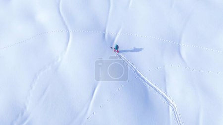 Téléchargez les photos : TOP DOWN : Voler au-dessus d'un trekking en pension fractionnée en montée par une journée ensoleillée d'hiver. Jeunes femmes en raquettes sur une colline enneigée lors d'un voyage hors piste de snowboard dans les montagnes slovènes idylliques. - en image libre de droit