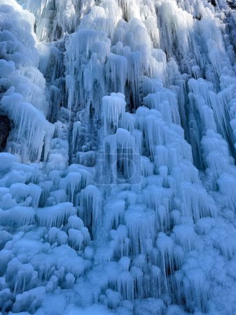 Foto de VERTICAL, CLOSE UP: Waterfall turns into a beautiful frozen wall of long white icicles in the sunny mountains of Slovenia. Close up view of the frozen formations from the bottom of a massive waterfall - Imagen libre de derechos