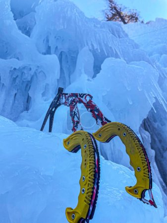 Téléchargez les photos : VERTICAL, BOTTOM UP, CLOSE UP: Two ice axes are stuck in the icicles of a massive frozen waterfall. Ice climbers leave their axes in the thick ice covering the rocky cliff. Ice climbing equipment. - en image libre de droit