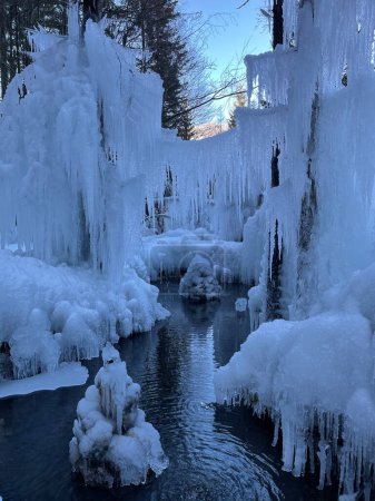 Foto de VERTICAL: Gorgeous hanging icicles and stunning ice formations surround a small mountain stream. Picturesque shot of formations of deep frozen ice surrounding a lazy river in Slovenian mountains. - Imagen libre de derechos