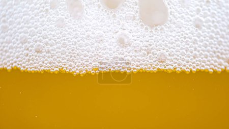 Foto de MACRO, DOF: Pequeñas burbujas forman la espuma encima de un vaso lleno de cerveza pálida. Primer plano de una pinta crujiente de cerveza dorada con espuma blanca perfecta. Macro detallado de una jarra espumosa de cerveza refrescante. - Imagen libre de derechos