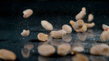 Photo for MACRO, DOF: Cinematic close up shot of a handful of salted peanuts getting scattered across the dining table. Organically grown salty peanuts fall out of a bag and onto the shiny kitchen countertop. - Royalty Free Image
