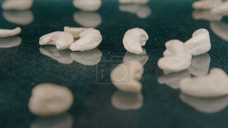 Foto de MACRO, DOF: A handful of cashews falls onto the polished surface of a dining table. Tasty cashew nuts get scattered across a shiny kitchen countertop. Organically grown Indian nuts bouncing off a desk - Imagen libre de derechos