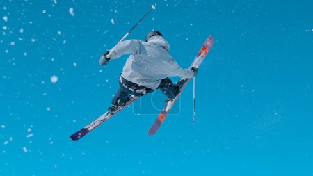 Foto de Athletic male tourist rides off a big snowpark kicker in Vogel and does a spectacular 360 grab. Expert freestyle skier rides up a kicker and does an awesome spinning trick on a sunny winter day. - Imagen libre de derechos