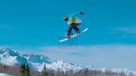 Photo for Spectacular shot of a snowboarding pro doing a rotating grab stunt while training in the scenic Vogel ski resort snowpark. Male snowboarder soars high through the air and does a breathtaking trick. - Royalty Free Image