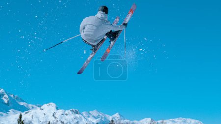 Téléchargez les photos : Male freestyle skier leaves a snow trail after taking off a kicker and doing a challenging 360 grab while riding in the snowpark of Vogel, Slovenia. Action shot of a man doing an extreme skiing trick. - en image libre de droit