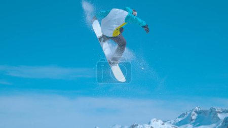 Foto de Snowboarder flies through the air and does a spinning nose grab while having fun in a snowpark in sunny Julian Alps. Awesome action shot of a man doing stunts while riding in Vogel snowboard park - Imagen libre de derechos
