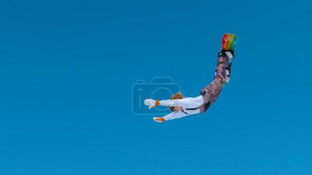 Photo for Extreme snowboarder catches big air and does a spectacular backflip with outstretched arms. Action shot of a stoked male tourist doing a tumbling trick while snowboarding in the scenic Julian Alps - Royalty Free Image