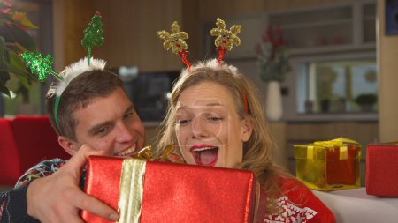 Téléchargez les photos : PORTRAIT, CLOSE UP: Cute Caucasian couple exchanging gifts on Christmas day. Beautiful young couple in love enjoying a fun Christmas day on a couch in their decorated home and giving gifts - en image libre de droit