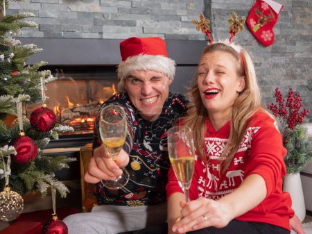 Foto de CLOSE UP PORTRAIT: Funny young couple getting drunk on champagne celebrating Christmas Eve. Goofy playful girlfriend and boyfriend toasting and drinking too much white wine on New Year's Eve - Imagen libre de derechos