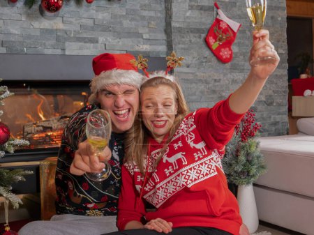 Foto de CLOSE UP PORTRAIT: Funny young couple getting drunk on champagne celebrating Christmas Eve. Goofy playful girlfriend and boyfriend toasting and drinking too much white wine on New Year's Eve - Imagen libre de derechos