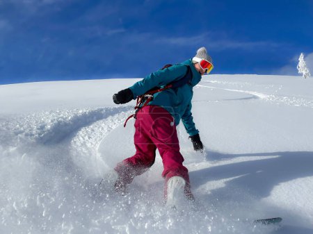 Téléchargez les photos : Woman on snowboarding vacation in Julian Alps smiles while shredding champagne powder. Cheerful female snowboarder sprays fresh powder snow while riding off-piste in the beautiful Slovenian mountains - en image libre de droit