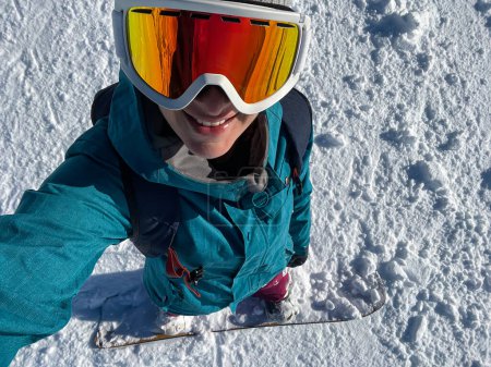Foto de SELFIE: Cheerful female snowboarder takes a selfie while riding in sunny backcountry covered in fresh snow. Young Caucasian woman smiles while snowboarding off piste in the pristine white Julian Alps. - Imagen libre de derechos