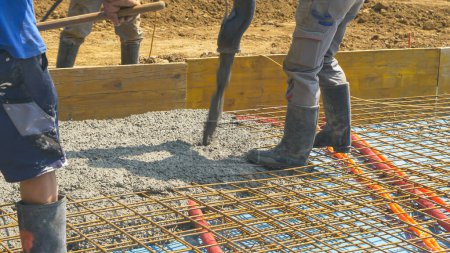 CLOSE UP: Builders pour the wet cement mixture over a layer of metal mesh. Contractors pour rough wet concrete over a reinforced steel net while creating the foundation of a modern housing projects.