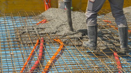 Photo for CLOSE UP: Contractors are pouring rough wet cement mixture while starting to build a house. Team of builders pours a concrete slab over the reinforced metal mesh as they create the foundation of house - Royalty Free Image