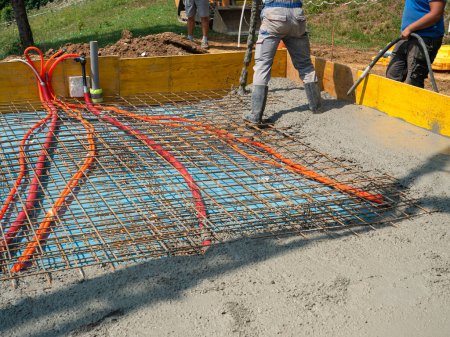 Foto de CLOSE UP: Male contractors are pouring a concrete slab while working at a modern housing project on a sunny summer day. Team of builders is pouring rough cement mixture and leveling a house foundation - Imagen libre de derechos