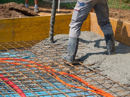 Téléchargez les photos : CLOSE UP: Team of builders is pouring rough cement mixture and leveling a house foundation. Male contractors are pouring a concrete slab while working at a modern housing project on a sunny summer day - en image libre de droit