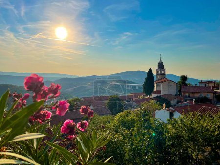 Téléchargez les photos : CLOSE UP, LENS FLARE: Golden summer sunbeams shine on the idyllic rural village of Crni Kal. Scenic view of blossoming pink flowers and the spectacular vista of the Crni Kal landscape and viaduct. - en image libre de droit