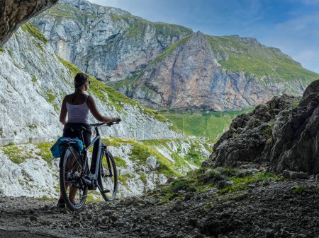 Téléchargez les photos : COPY SPACE: Young woman cycling in the Slovenian mountains stops at a scenic viewpoint on an idyllic summer day. Female tourist mountain biking near Mangart observes the stunning nature of Slovenia. - en image libre de droit