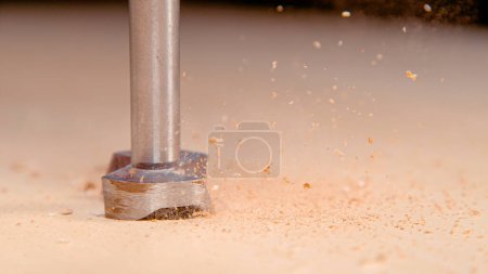 Photo for MACRO, COPY SPACE, DOF: Carpenter's modern drill bores a wide hole into a wooden board. Detailed shot of sawdust flying into the air as a handheld industrial power tool drills a hole in the wood. - Royalty Free Image
