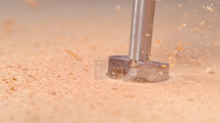 Téléchargez les photos : MACRO, DOF: Tiny particles of wood fly into the air as a silver drill bores a hole into the board. Wood chippings fly off the spinning handheld drill boring a wide hole in a thick piece of timber. - en image libre de droit