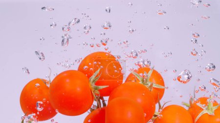 Photo for UNDERWATER, CLOSE UP: Ripe cherry tomatoes fall into a large container full of cold water. Cinematic close up view of small sweet tomatoes as they fall into the crystal clear water. Salad ingredient. - Royalty Free Image
